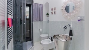 Une salle de bain moderne avec une douche à parois de verre, des toilettes blanches, un lavabo doté d’un grand bac et un miroir décoratif.