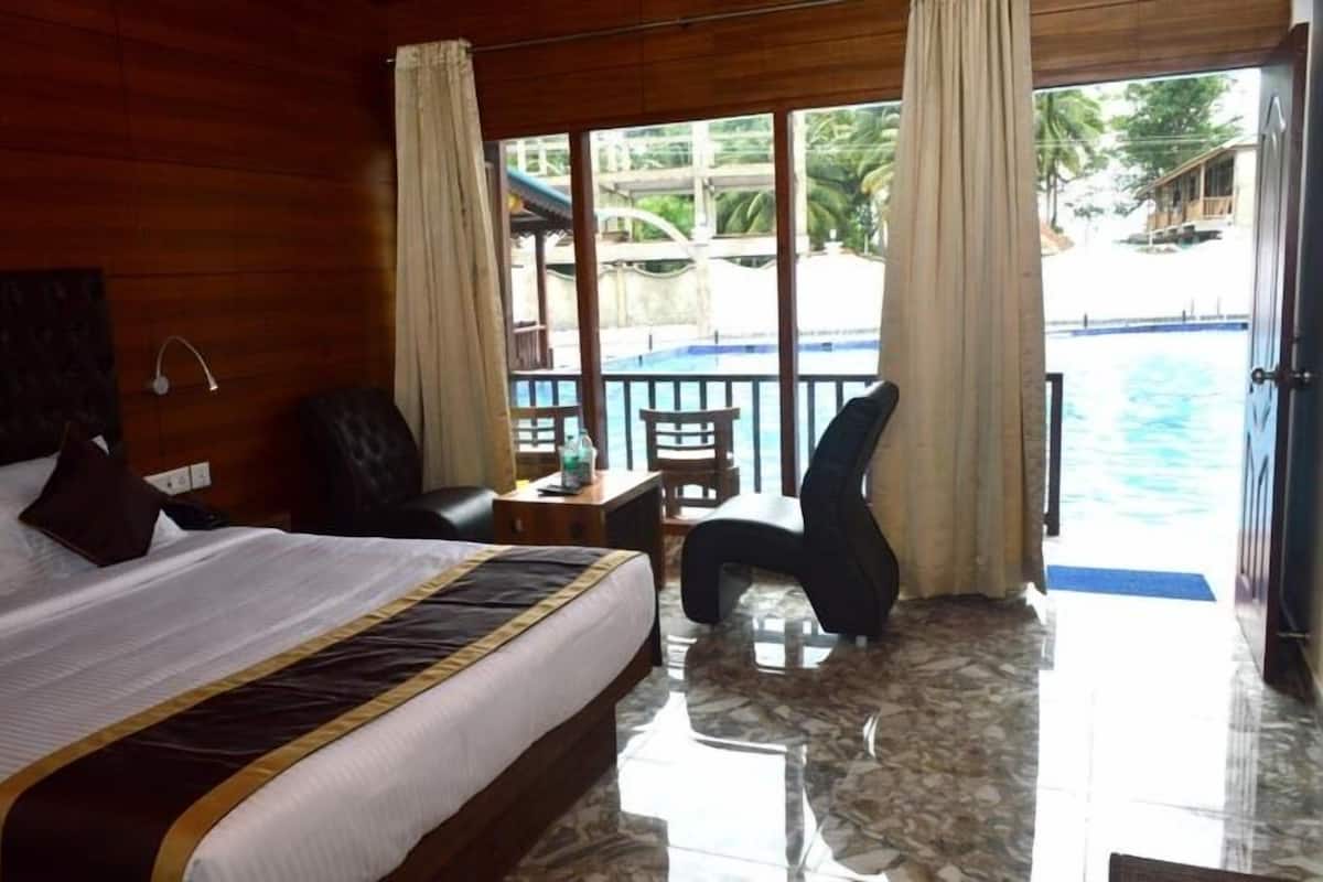 A hotel room with a bed, a chair, a small table, and a view of a pool.