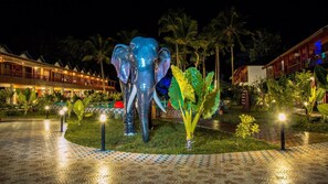 A large elephant sculpture in a well-lit garden area with palm trees and a pool in the background. - Aquays Hotels & Resorts (Port Blair)