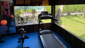 Un gimnasio con equipo de ejercicio, una cinta de correr y un amplio ventanal con vistas al verdor.