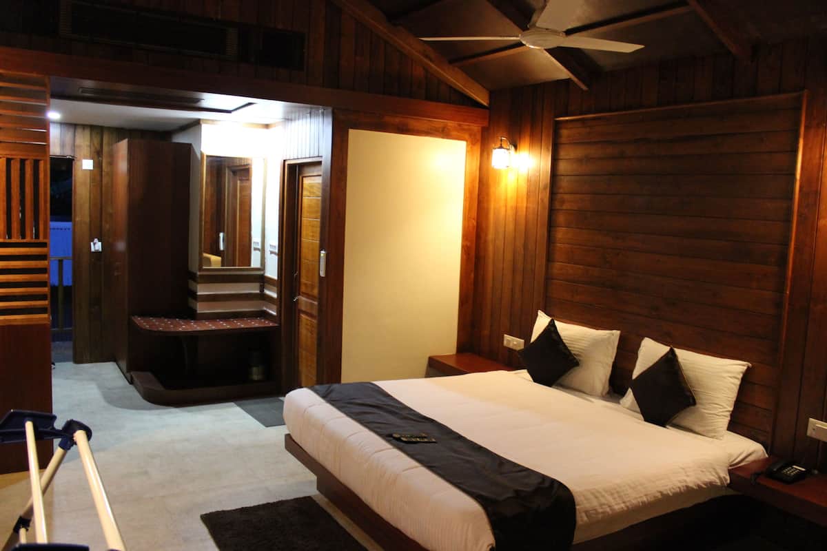 A bedroom with a large bed, wooden walls, a ceiling fan, and a small seating area.