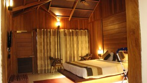 Una habitación tipo cabaña de madera con una cama, dos sillas, una mesita y un ventilador de techo.