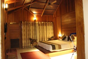 Um quarto no estilo de cabana de madeira, com uma cama, duas cadeiras, uma mesinha e um ventilador de teto.