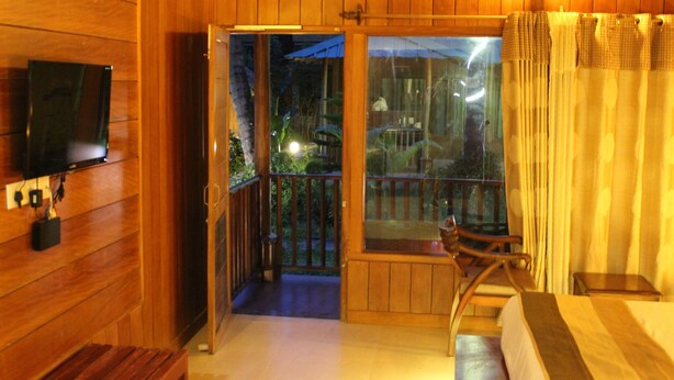 Una habitación de madera con televisión en la pared, un balcón con vistas al jardín y una cama con cabecera de madera.
