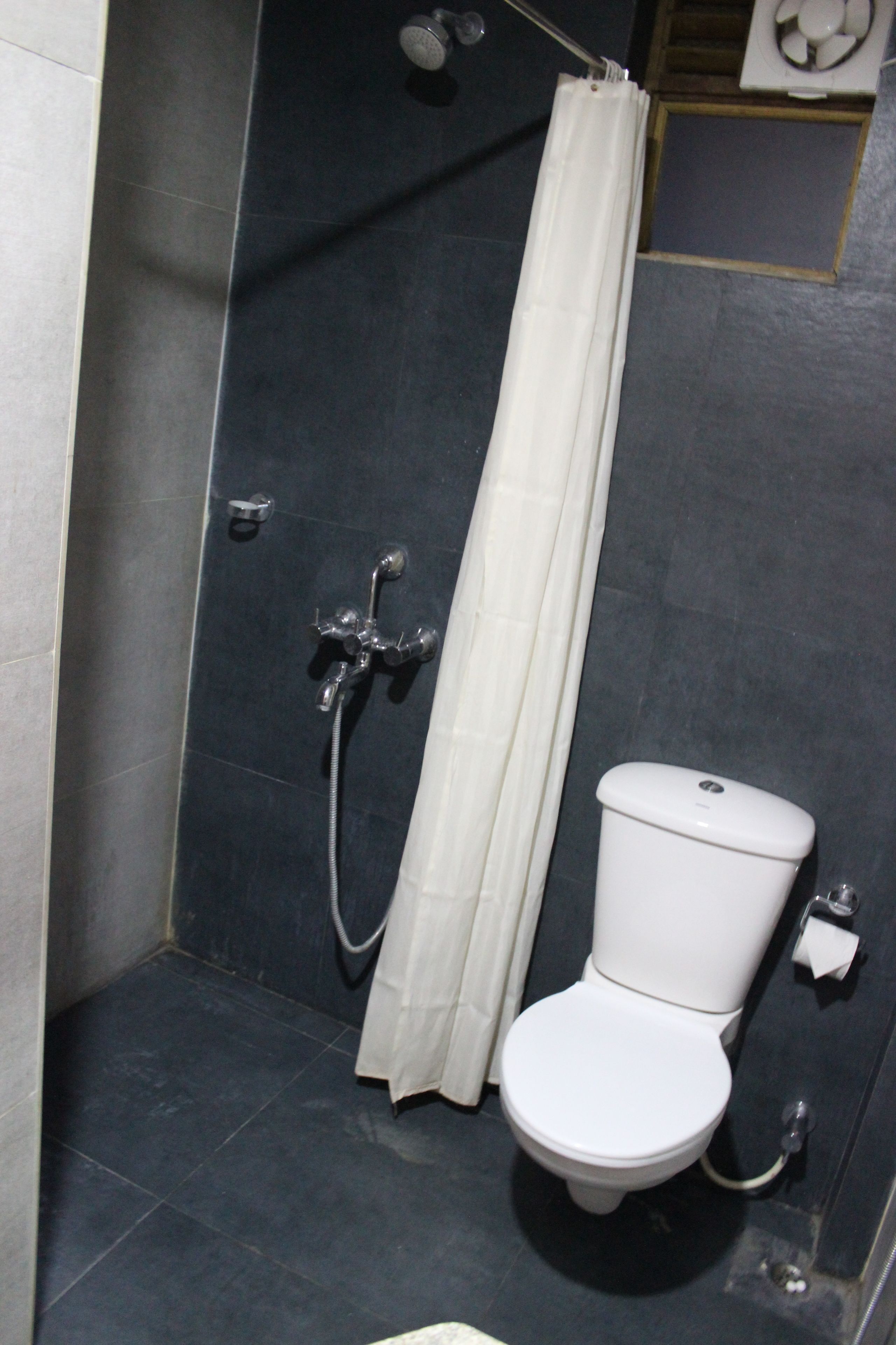 Un baño pequeño con azulejos oscuros, ducha, inodoro y un perchero para toallas.
