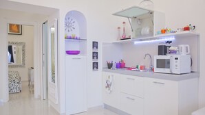 A modern kitchen with white cabinets, a microwave, and a sink. There is a decorative clock on the wall and a bowl on the counter.