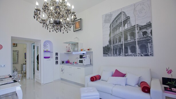 A modern living room with a white sofa, a chandelier, a kitchen area, and a large photo of a historical building.