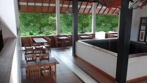 Un espacio al aire libre techado con mesas y sillas de madera, una piscina y vistas a zonas verdes.