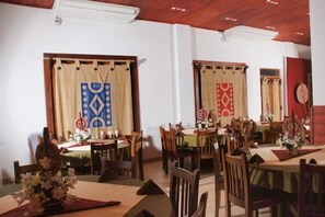 A dining area with multiple tables and chairs, wooden ceiling, and curtains with geometric patterns.
