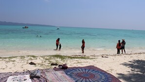 Una playa con gente cerca del agua, un bote y una manta en la arena.
