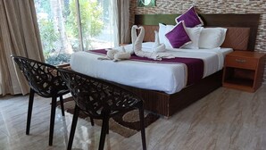 Habitación de hotel con cama, dos sillas, una mesita de noche y vistas a zonas verdes por la ventana.