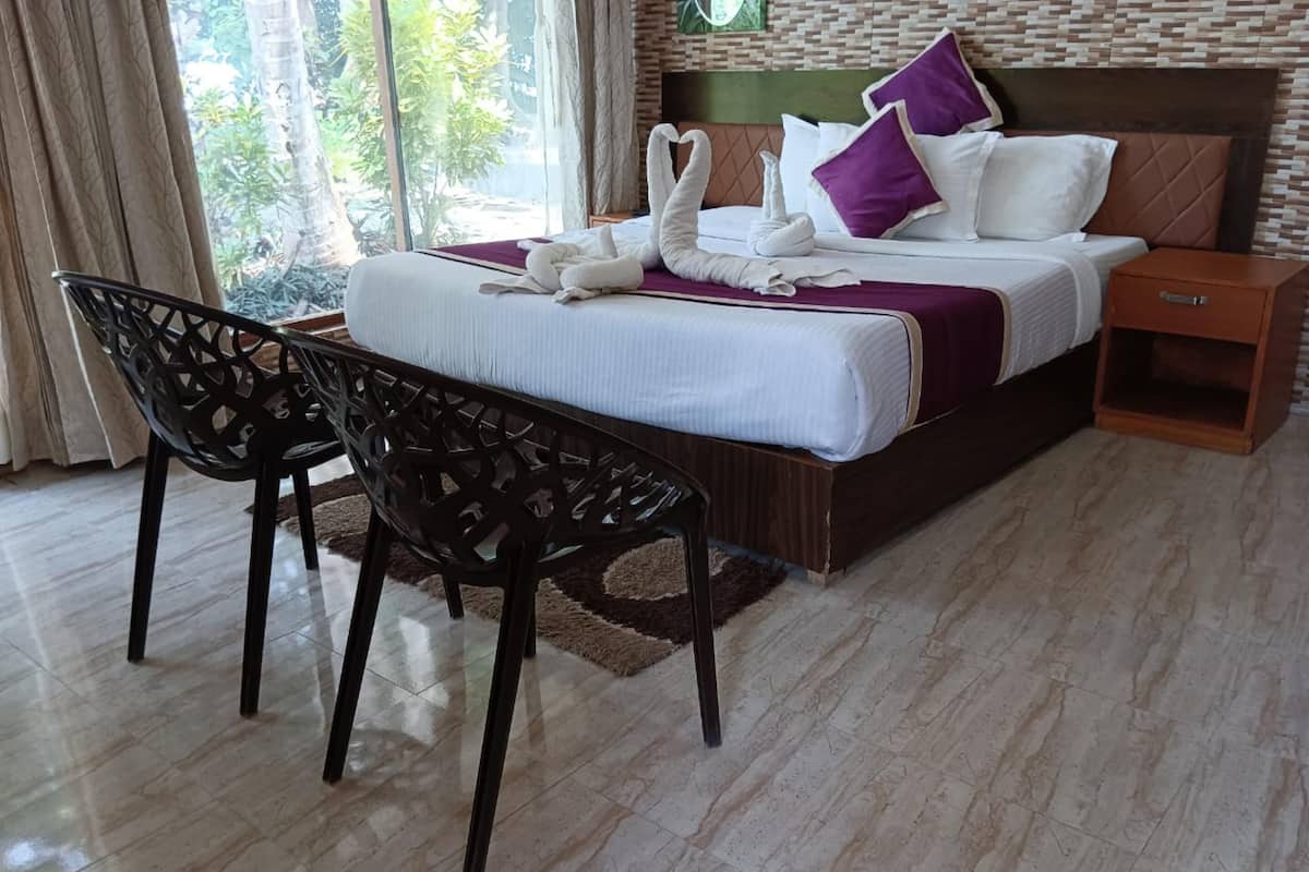 A hotel room with a bed, two chairs, a nightstand, and a view of greenery through the window.