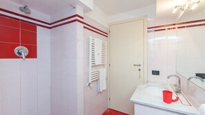 Een badkamer met gestreepte tegels, een douche, een toilet en een wastafel met een rode zeepbak.