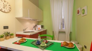 Een kleine keuken met een spoelbak, magnetron en een klok aan de muur.