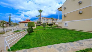 A courtyard with a stone pathway, a white railing, and a well-maintained lawn with palm trees. - Gold Lion Apart Hotel (Fethiye)