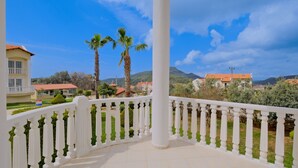 A balcony with white balustrades, a tiled floor, and a view of houses and palm trees in the background. - Gold Lion Apart Hotel (Fethiye)