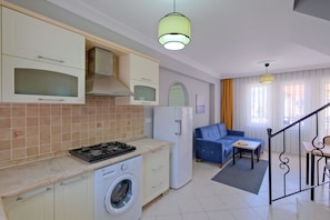 A compact kitchen with a washing machine, a dining area with a table and chairs, and a living area with a sofa. - Gold Lion Apart Hotel (Fethiye)