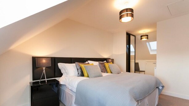 A modern bedroom with a large bed, a nightstand, a lamp, and a skylight. - The Townhouse (Derby)