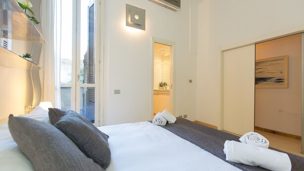 A hotel room with a bed, pillows, a towel, a mirror, and a painting on the wall.