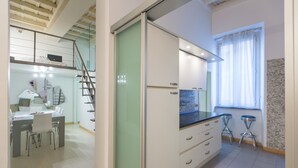 A modern kitchen with a dining area, a staircase, and a window with curtains.