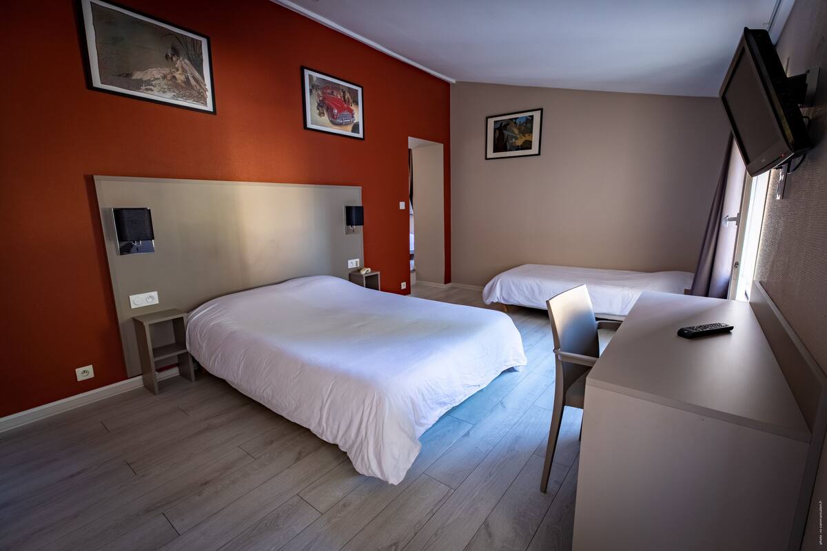 A hotel room with two beds, a desk, and a TV.