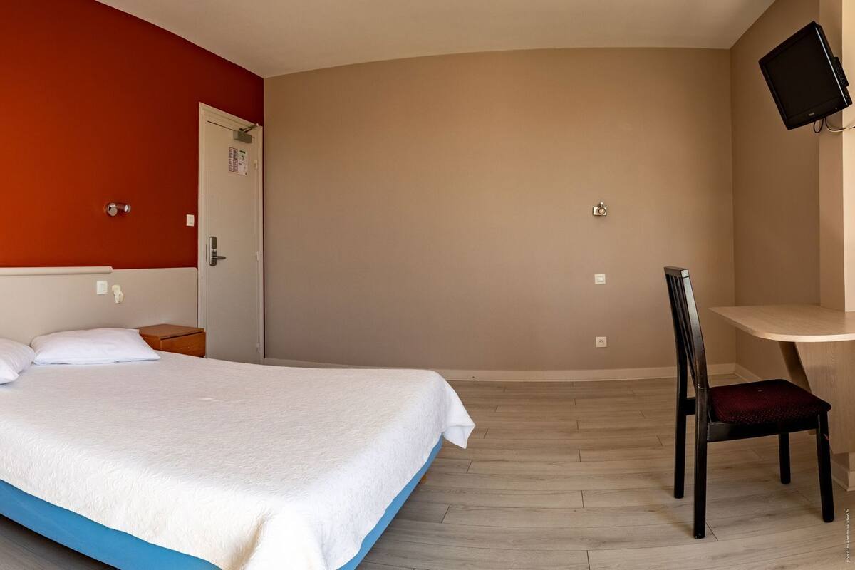 A bedroom with a bed, bedside tables, a desk, a chair, and a TV mounted on the wall.