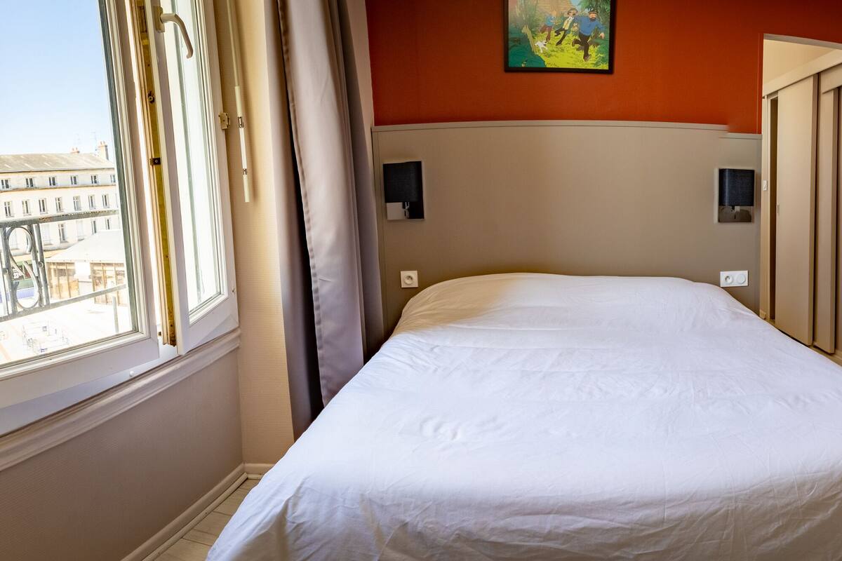A hotel room with a large bed, a smaller bed, a window with curtains, and a painting on the wall.