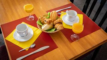 Ein Frühstückstisch mit Croissants, Orangensaft und Kaffee auf einer Holztischplatte mit roter Unterlage.