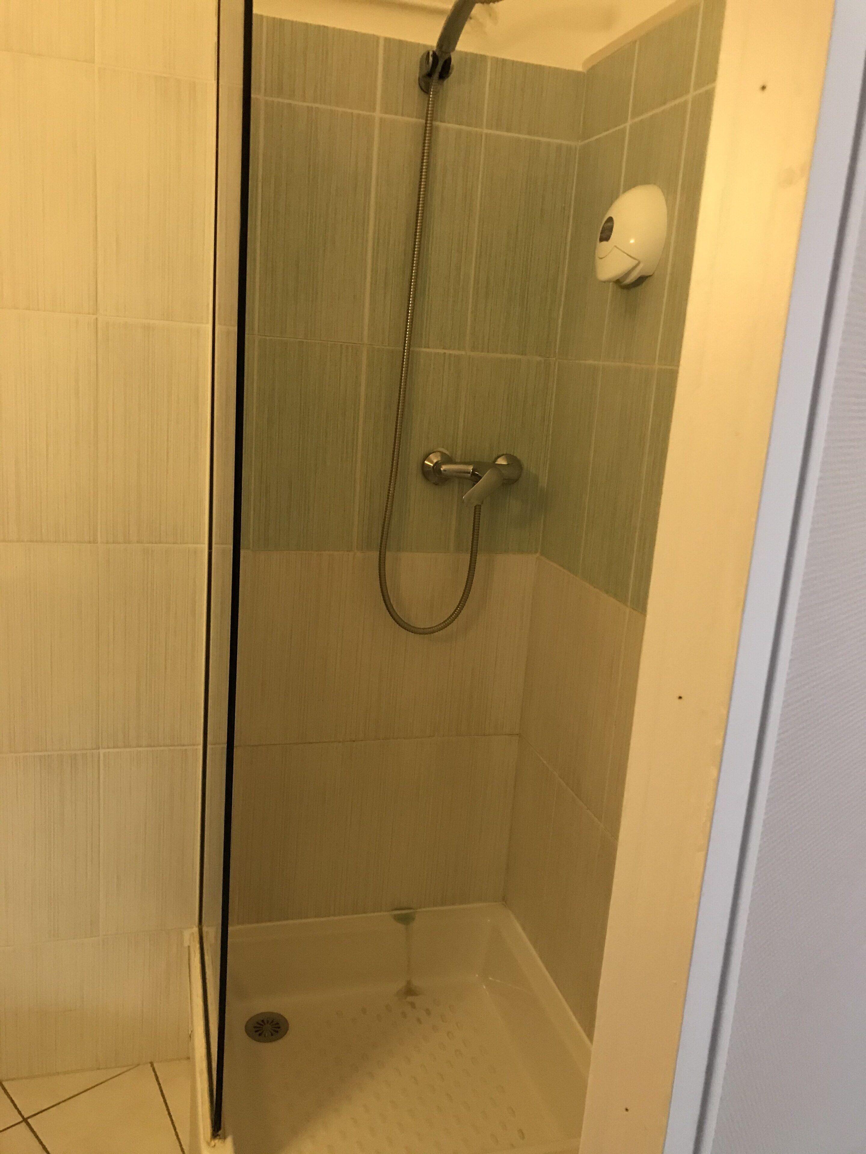 A small, enclosed shower area with a handheld showerhead and a wall-mounted soap dispenser.