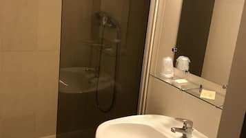Un baño con ducha de vidrio, un lavamanos blanco y un espejo con repisa de vidrio arriba.