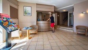 A reception area with a desk, chairs, a display of brochures, and a staircase leading to another floor. - Hotel de la Gare – urban by balladins (Chateauroux)