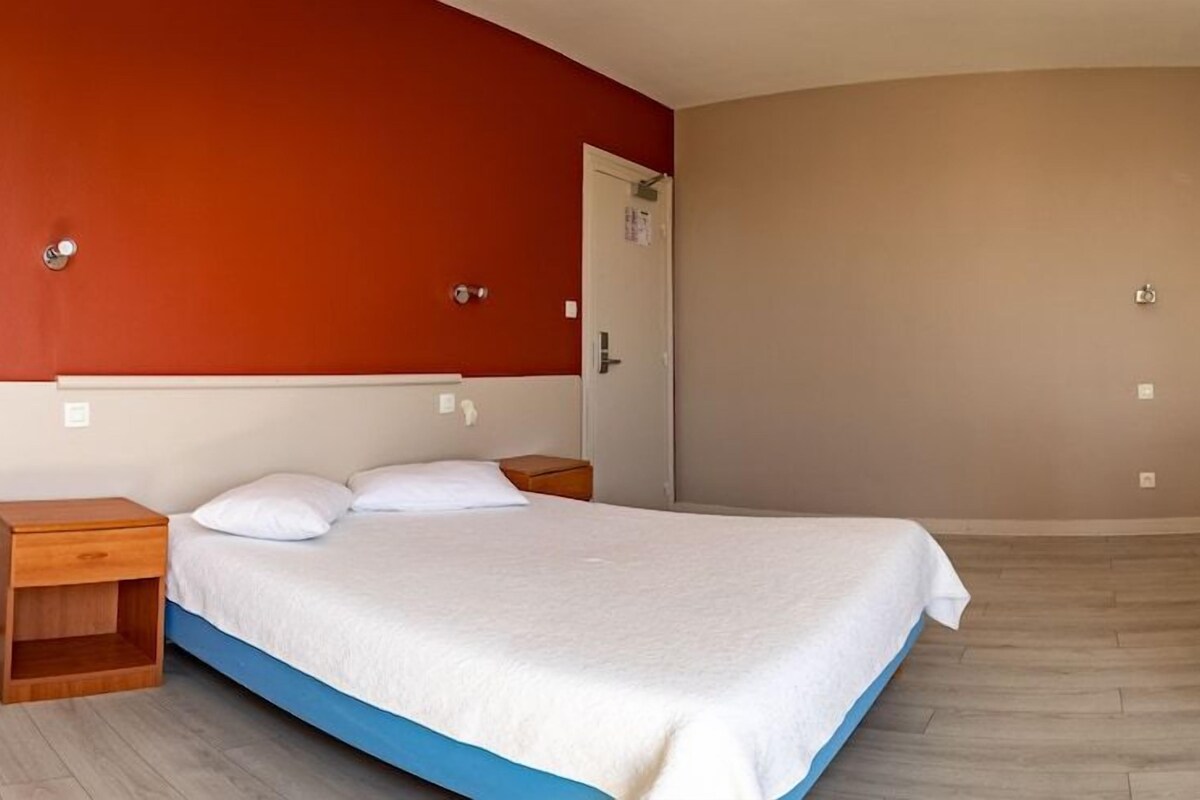 Un dormitorio con cama, mesitas de noche, una silla y televisor montado en la pared.