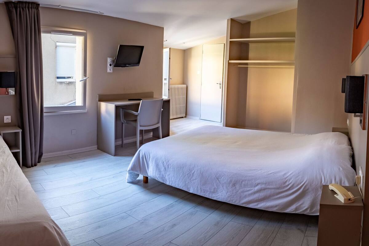 A hotel room with two beds, a desk, a chair, a TV, and a wardrobe.