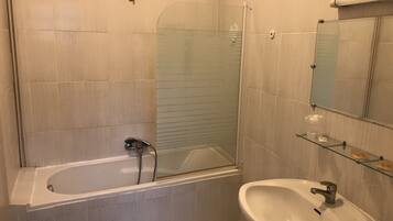 A bathroom with a bathtub, a sink, a glass shower enclosure, and a mirror.