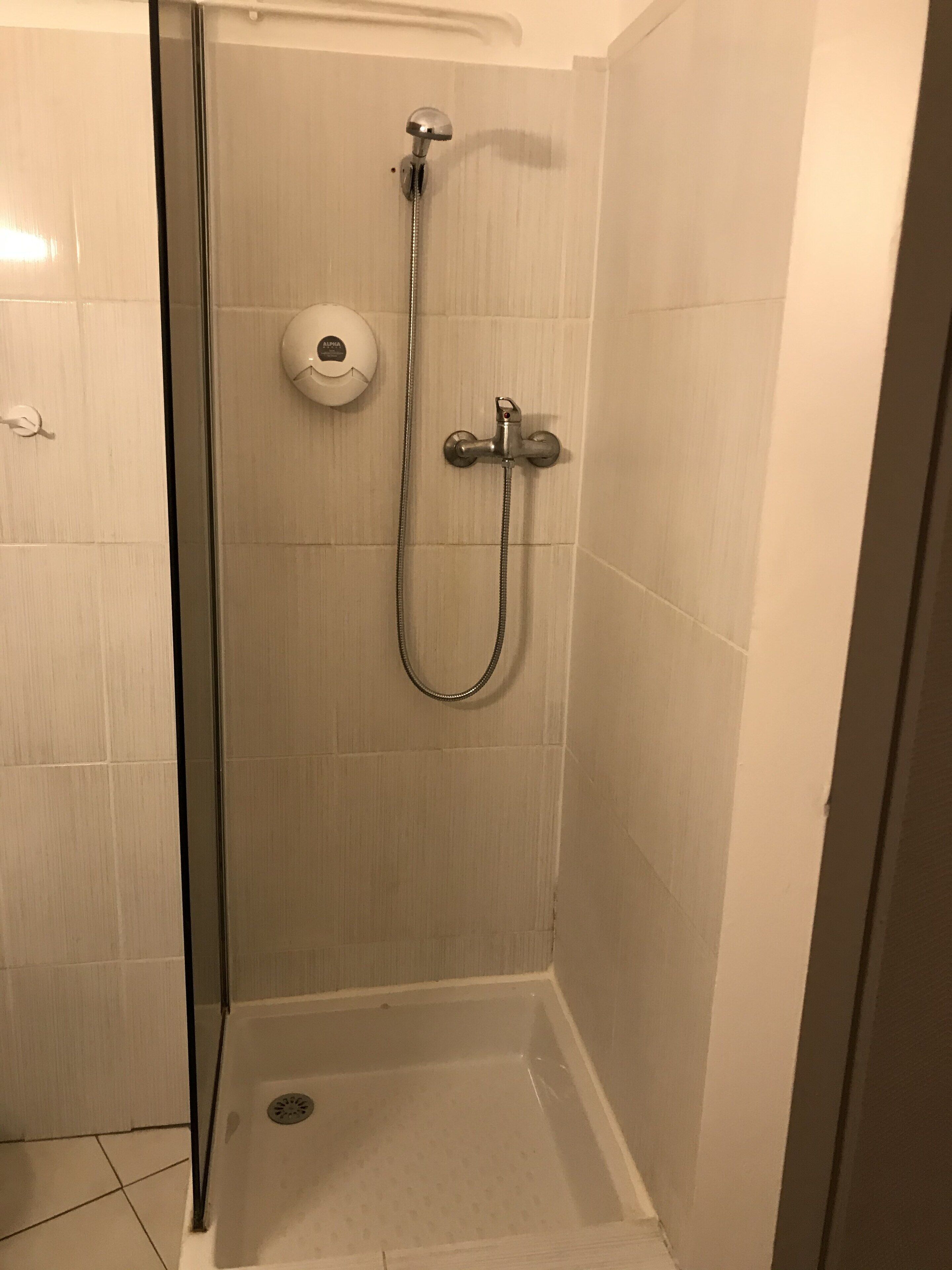 A small, enclosed shower area with a handheld showerhead and a wall-mounted faucet.