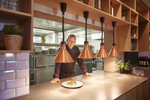 Uma cozinha moderna com luminárias pendentes em cobre, um chef no balcão e um prato de comida bem organizado.