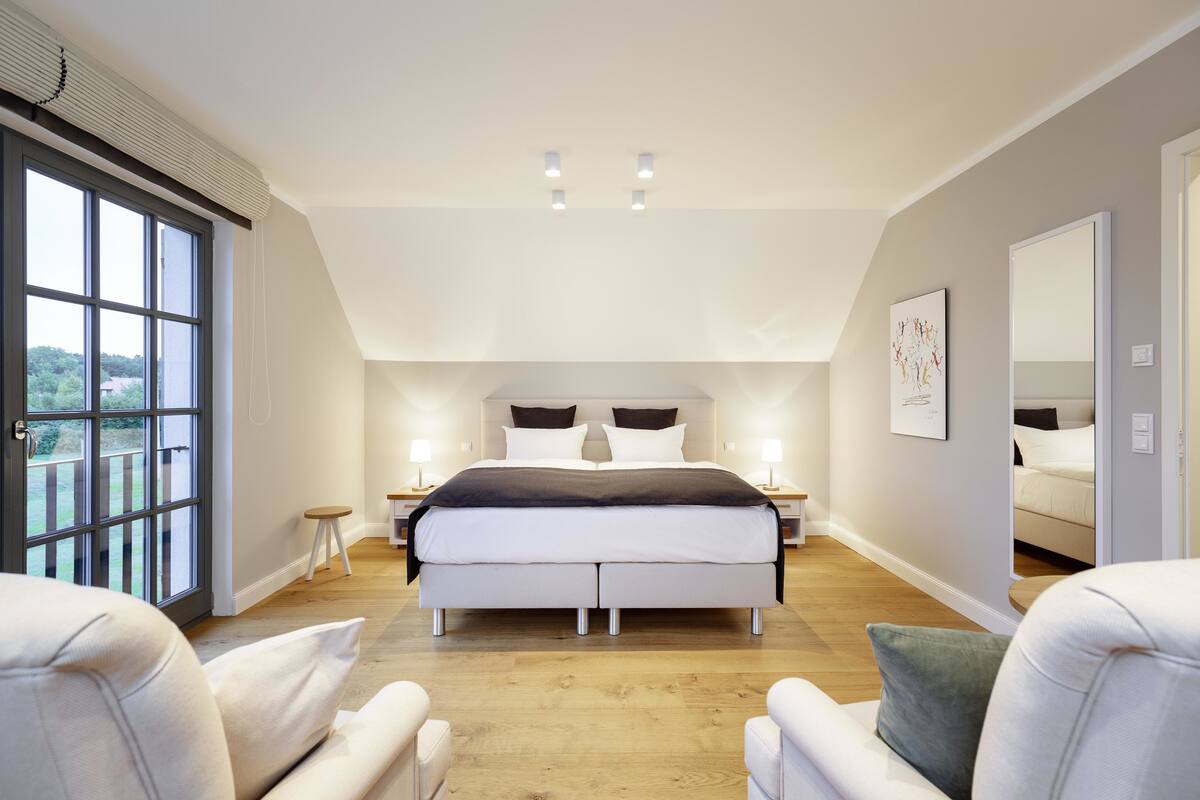 A bedroom with a large bed, two bedside tables, a window, and a mirror.