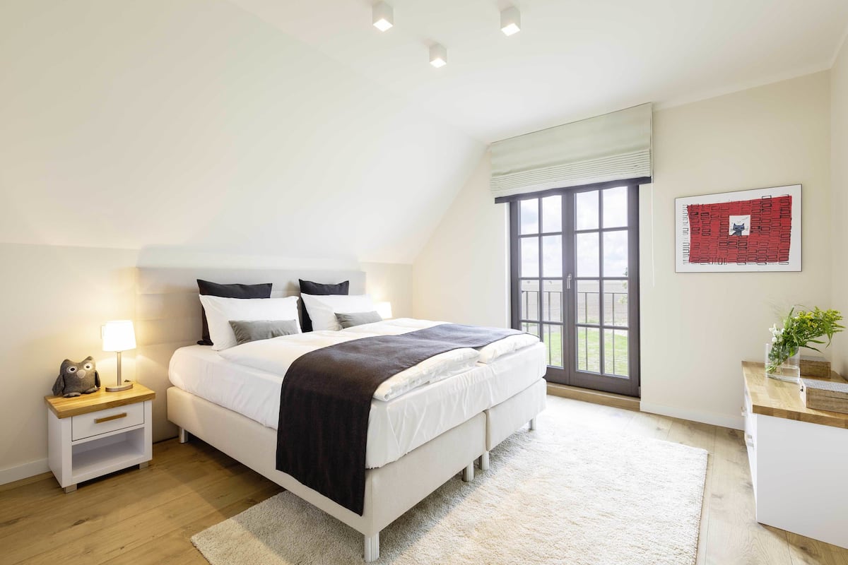 A bedroom with a bed, bedside table, lamp, and a window with a view.