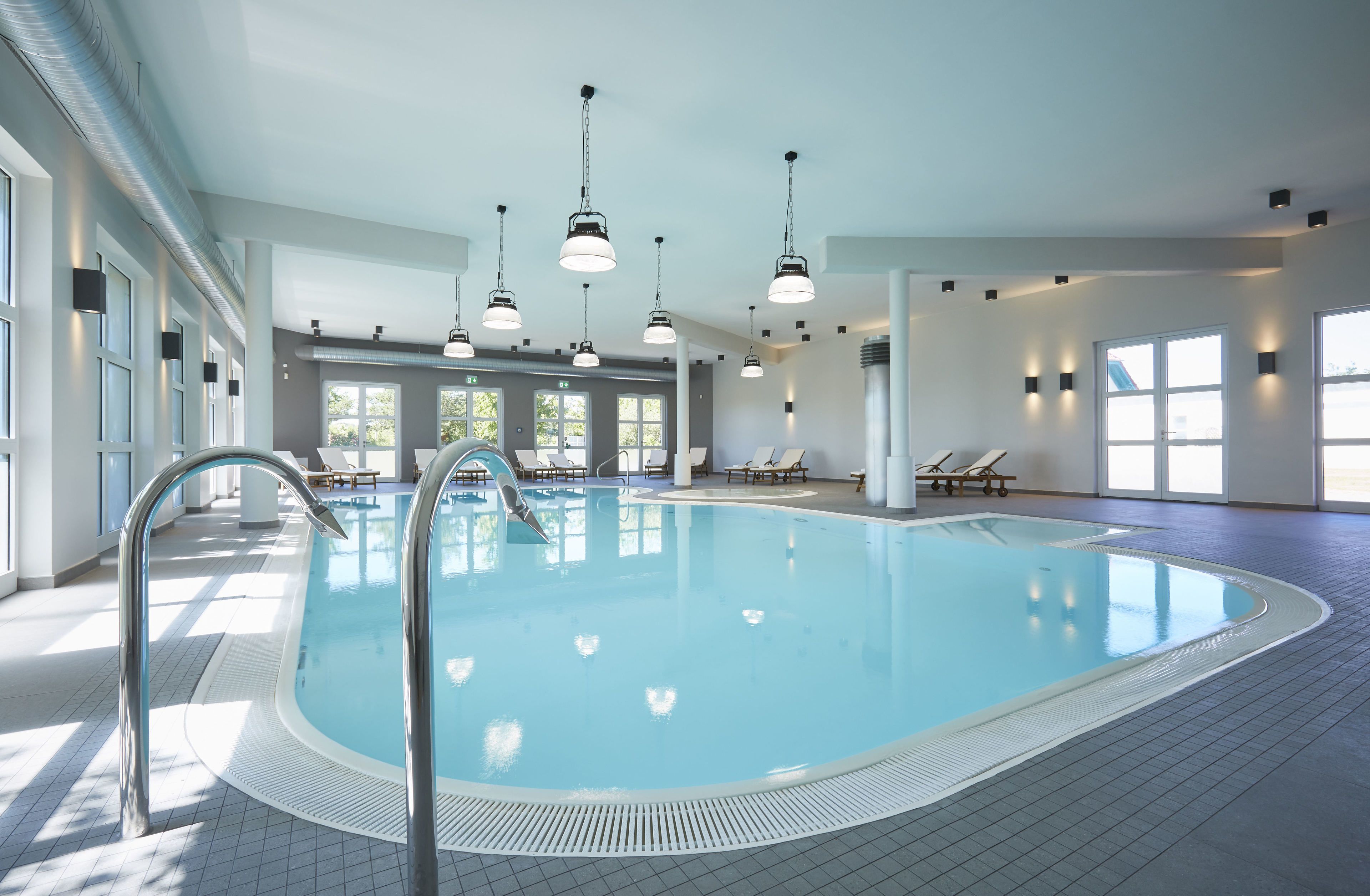 An indoor swimming pool with clear water, surrounded by lounge chairs and a tiled floor.