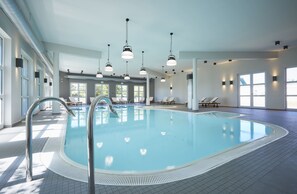 Piscina interna com água cristalina, rodeada por cadeiras de descanso e piso em azulejo.