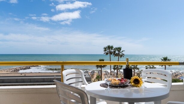 Une table avec un verre de vin, une assiette de nourriture et un tournesol, le tout sur un balcon donnant sur la plage.