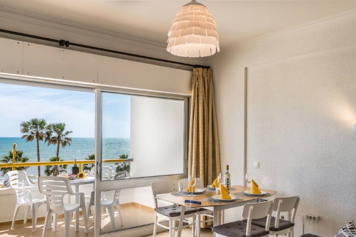 Un balcon avec vue sur la mer, une table à manger avec des chaises, et un luminaire suspendu.