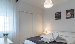 A hotel room with a bed, a bedside table with a lamp, a potted plant, and two wall art pieces. - Akisol Quarteira Ocean (Loulé)