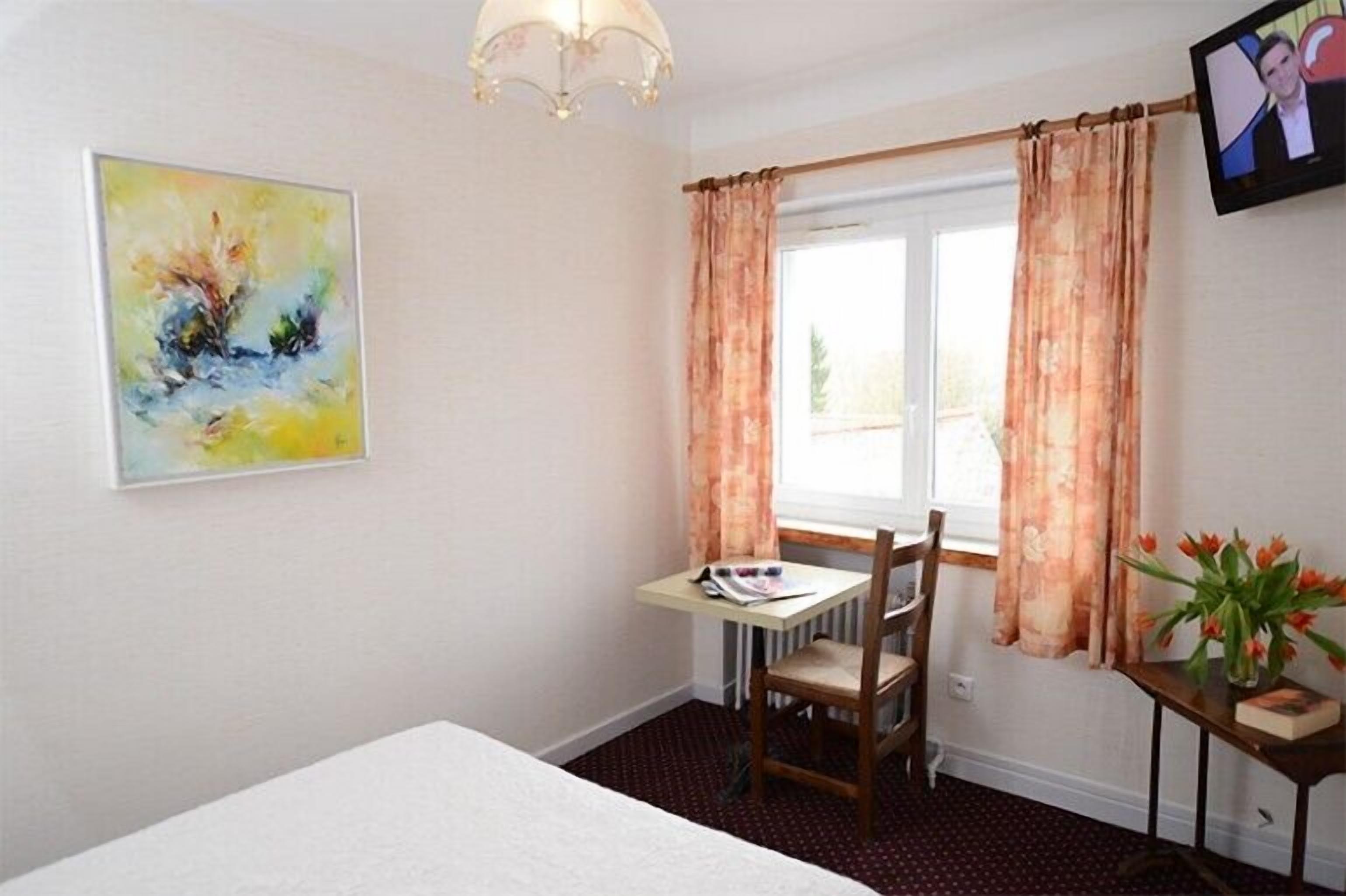 A room with a bed, a desk with a chair, a window with curtains, a painting on the wall, and a television on the wall.