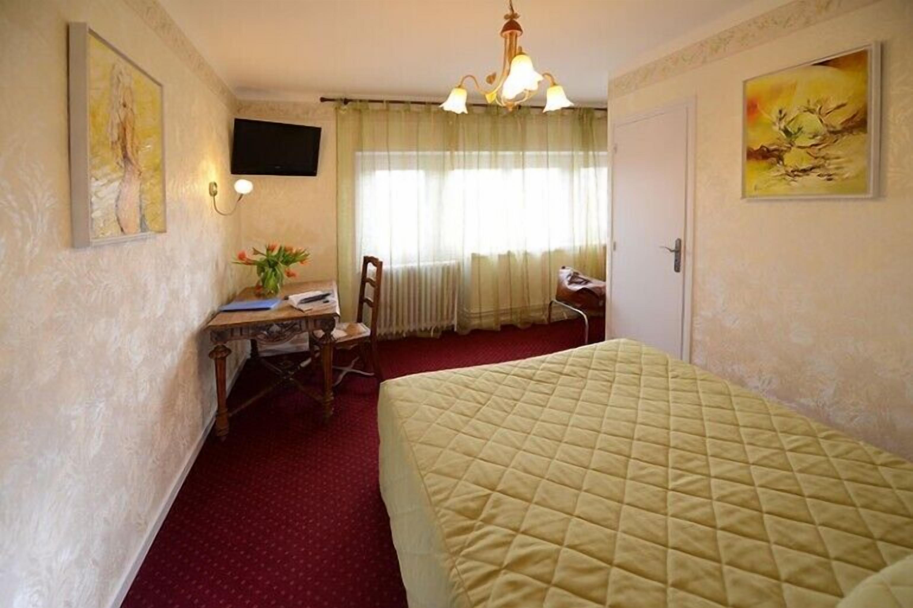 A hotel room with a bed, a desk, a chair, a television, and a window with curtains.