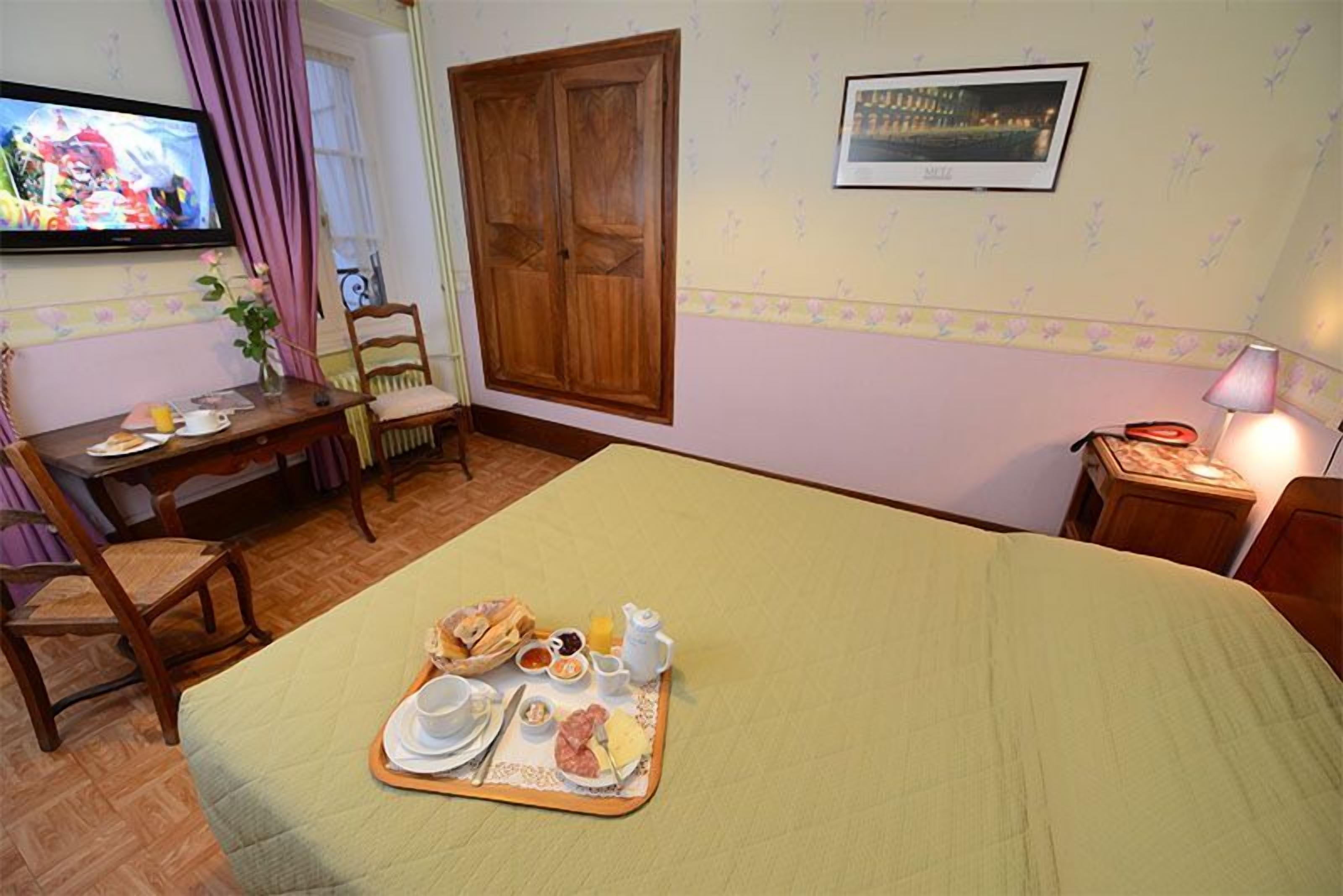 A hotel room with a bed, breakfast tray, TV, wooden wardrobe, and a framed picture on the wall.
