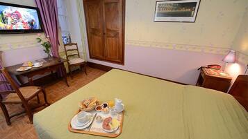 A hotel room with a bed, breakfast tray, TV, wooden wardrobe, and a framed picture on the wall.