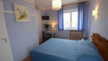 A bedroom with a large bed, a desk with a chair, a television, and a window with curtains.