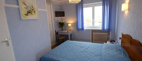 A bedroom with a large bed, a desk with a chair, a television, and a window with curtains.