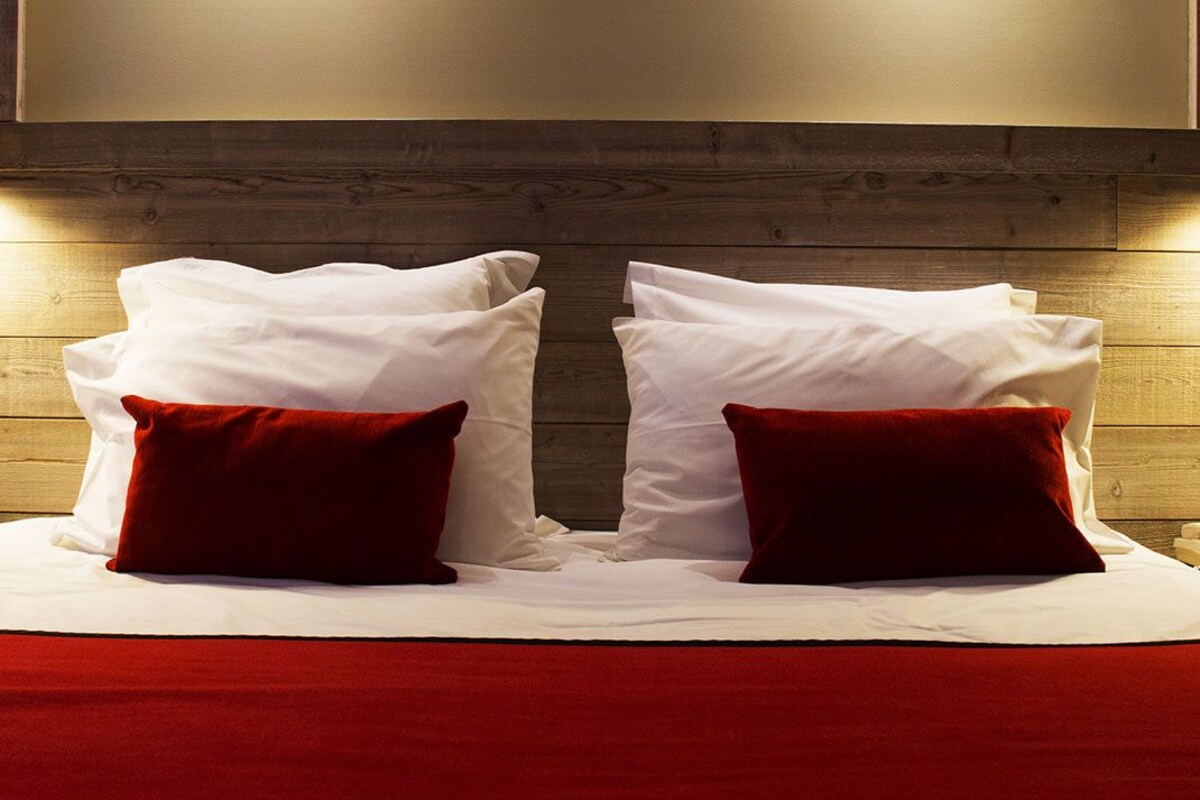 A bed with white linens and two red pillows, set against a wooden headboard.